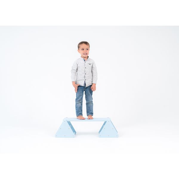 Balance constructor, blue. The boy is standing on the balance constructor, the board is placed at the highest level, straight.